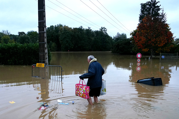 Un habitant porte des sacs en marchant dans une rue inondée à Pommeuse, en Seine-et-Marne, le 10 octobre 2024. (DIMITAR DILKOFF/AFP via Getty Images)