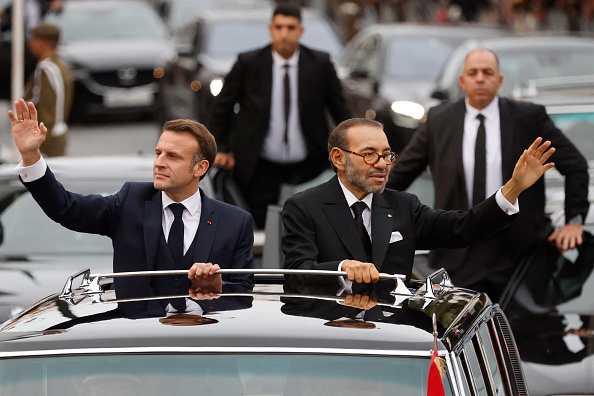 Le roi du Maroc Mohammed VI et le président Emmanuel Macron saluent la foule alors qu'ils roulent sur une route de la capitale Rabat, le 28 octobre 2024. (LUDOVIC MARIN/POOL/AFP via Getty Images)