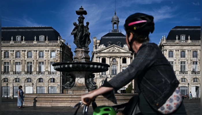 Une femme passe à vélo devant la fontaine "Des Trois Grâces", place de la Bourse, à Bordeaux. (Photo  : PHILIPPE LOPEZ/AFP via Getty Images)