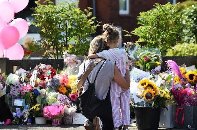 Une mère serre son enfant dans ses bras alors qu'ils regardent les hommages rendus aux victimes d'une attaque meurtrière au couteau à Southport, dans le nord-ouest de l'Angleterre, le 31 juillet 2024, qui a coûté la vie à trois petites filles. La police avait déclaré qu'elle ne considérait pas l'attaque comme liée au terrorisme. (PETER POWELL/AFP via Getty Images)