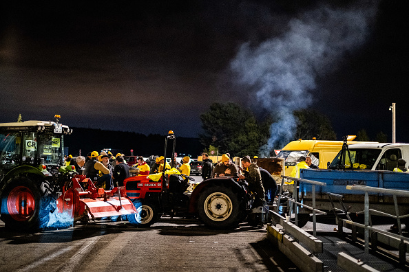 Blocage d'autoroute avec tracteurs et agriculteurs au crépuscule devant des camions bloqués sur l'autoroute A9 au péage du Boulou dans le département des Pyrénées-Orientales dans le sud de la France le 19 novembre 2024. (JC MILHET/Hans Lucas/AFP via Getty Images)