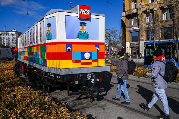 Des visiteurs observent le tramway grandeur nature construit à partir de briques Lego classiques sur la place Deak Ferenc, dans le centre de Budapest, le 21 novembre 2024. Le tram a été conçu par l'artiste visuel Balazs Doczy, basé à Budapest. (ATTILA KISBENEDEK/AFP via Getty Images)