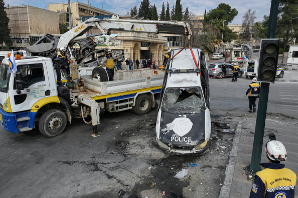 Des membres du service de défense civile syrien des Casques blancs en train de dégager des carcasses de véhicules et des décombres dans une rue d'Alep, le 5 décembre 2024. (OMAR HAJ KADOUR/AFP via Getty Images)