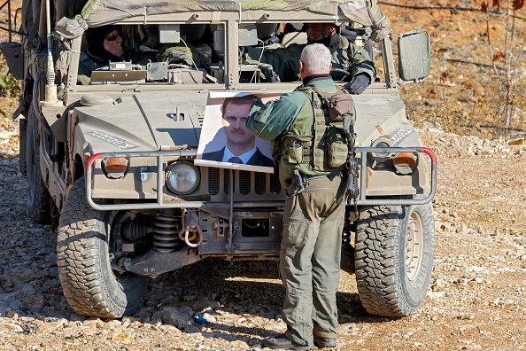 Un soldat de l'armée israélienne tient un portrait du président syrien évincé Bachar al-Assad à côté d'un véhicule humvee près du village druze de Majdal Shams sur les hauteurs du Golan le 14 décembre 2024. (JALAA MAREY/AFP via Getty Images)