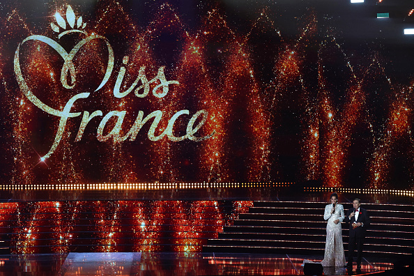 La directrice de l'organisation Miss France et Miss France 2005, Cindy Fabre et l'animateur Jean-Pierre Foucault s'expriment sur scène lors du concours de beauté Miss France 2025 à l'Arena Futuroscope de Chasseneuil-du-Poitou, le 14 décembre 2024.   (ROMAIN PERROCHEAU/AFP via Getty Images)