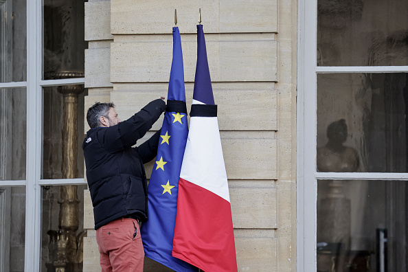 Un membre du personnel attache des rubans noirs sur le drapeau de l'Union européenne et le drapeau français à l'hôtel Matignon, le 23 décembre 2024. (STEPHANE DE SAKUTIN/AFP via Getty Images)