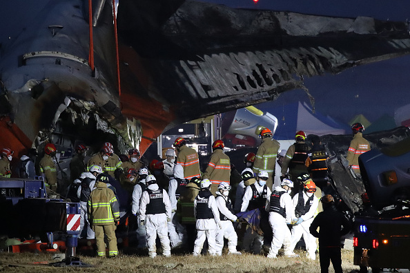 Des pompiers transportent le corps d'un passager hors de l'épave de l'avion crashé à l'aéroport international de Muan, le 29 décembre 2024 à Muan-gun, en Corée du Sud. (Photo Chung Sung-Jun/Getty Images)