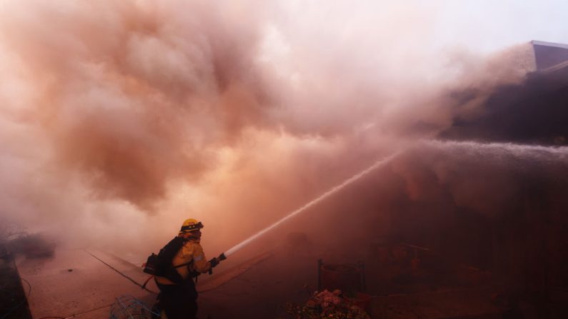 Des pompiers s'efforcent d'éteindre les flammes qui engloutissent une maison alors qu'un feu de broussailles fait rage à Pacific Palisades, en Californie, le 7 janvier 2025. (David Swanson/AFP via Getty Images)