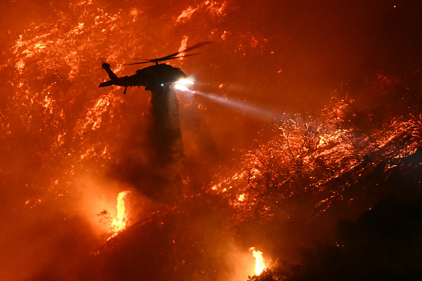 Un hélicoptère de lutte contre les incendies largue de l'eau alors que l'incendie des Palisades prend de l'ampleur près du quartier de Mandeville Canyon et d'Encino en Californie, le 11 janvier 2025. (Photo PATRICK T. FALLON/AFP via Getty Images)