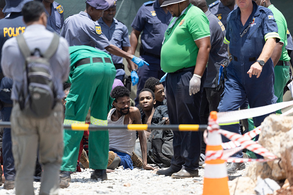 Des mineurs illégaux secourus d'une mine d'or abandonnée sont assis sur le sol à Stilfontein, le 14 janvier 2025. (CHRISTIAN VELCICH/AFP via Getty Images)