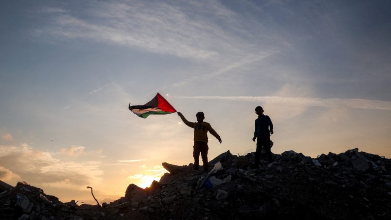 Un garçon court avec un drapeau palestinien sur un monticule de décombres dans un camp pour populations déplacées par le conflit à Bureij, dans le centre de la bande de Gaza, le 17 janvier 2025, suite à l'annonce d'une trêve dans le cadre de la guerre entre Israël et le Hamas. (EYAD BABA/AFP via Getty Images)