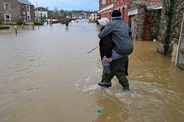 Un homme porte une personne sur son dos alors qu'ils traversent une route inondée suite au débordement de la Vilaine, à Pont-Rean, le 27 janvier 2025. (Photo DAMIEN MEYER/AFP via Getty Images)