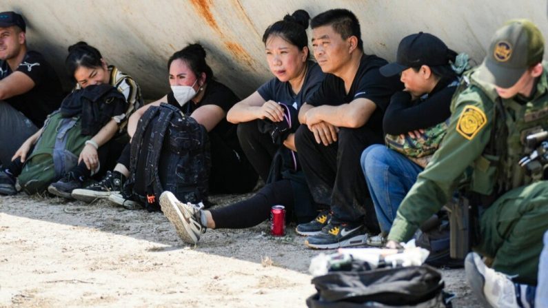 Des immigrants clandestins chinois attendent pendant qu'un agent de la Border Patrol prodigue des soins médicaux à une femme au milieu d'un grand groupe d'immigrés clandestins près d'Eagle Pass, au Texas, le 20 mai 2022. (Charlotte Cuthbertson/Epoch Times)