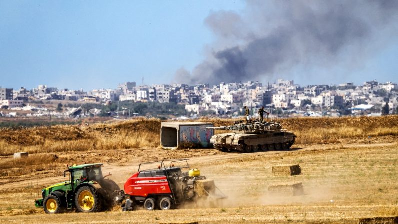 Un véhicule agricole récolte du foin près d'un char de combat de l'armée israélienne alors que de la fumée s'élève au-dessus de la bande de Gaza, près de la frontière avec Gaza, en Israël, le 15 mai 2024. (Jack Guez/AFP via Getty Images)