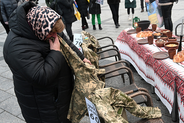 Une femme embrasse l'uniforme de son fils, en captivité depuis 680 jours, alors qu'elle se tient à côté d'une table de Noël symbolique composée de plats traditionnels, lors d'un rassemblement de soutien aux prisonniers de guerre et aux soldats disparus à Lviv, le 21 décembre 2024, dans le contexte de l'invasion russe de l'Ukraine. (YURIY DYACHYSHYN/AFP via Getty Images)