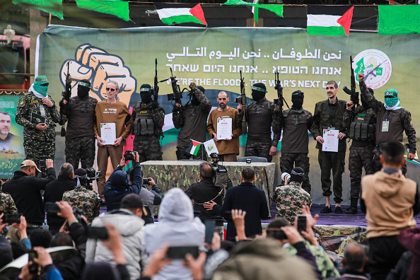 Des terroristes palestiniens du Hamas escortent les otages israéliens (de g. à dr., détenant des certificats) Ohad Ben Ami, Eli Sharabi et Or Levy sur une scène avant de les remettre à une équipe de la Croix-Rouge à Deir el-Balah, le 8 février 2025. (BASHAR TALEB/AFP via Getty Images)