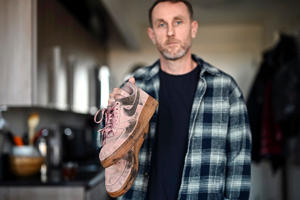 Joseph Lynskey, qui a survécu après avoir été poussé sur les voies du métro devant un train qui arrivait en sens inverse le 31 décembre 2024, tient les chaussures qu'il portait ce jour-là, à New York, le 4 février 2025. Joseph Lynskey attendait tranquillement une rame de métro new-yorkaise la veille du Nouvel An lorsqu'il a été poussé par derrière sur les voies au moment où un train entrait en gare. « J'ai su instantanément que quelqu'un m'avait poussé et avait essayé de me tuer », a déclaré le producteur de musique à l'AFP. (ANGELA WEISS/AFP via Getty Images) 