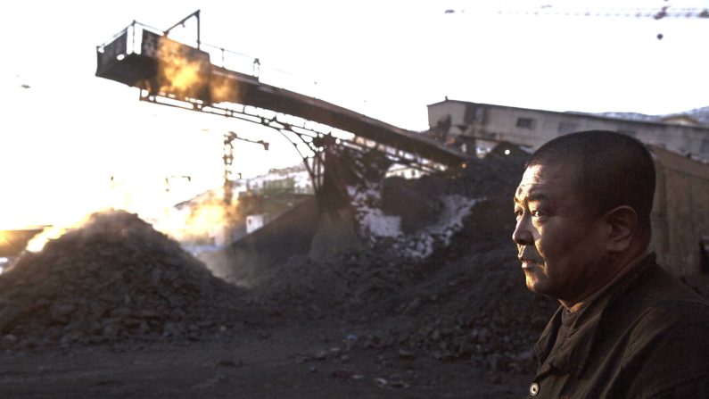 Un ouvrier minier chinois regarde le charbon se déplacer sur un tapis roulant dans une zone de triage d'une mine de charbon, le 25 novembre 2015 à Shanxi, en Chine. (Kevin Frayer/Getty Images)