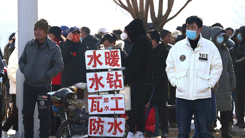 Le 6 février 2023, des travailleurs migrants attendent d'être embauchés dans une rue de Shenyang, dans la province du Liaoning, dans le nord-est de la Chine, devant des panneaux vantant leurs compétences. (STR/AFP via Getty Images)