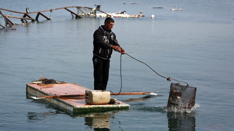 Un Palestinien se tient sur la porte d'un réfrigérateur qu'il utilise comme embarcation de fortune, alors qu'il jette son panier de pêche à la mer dans le port de Gaza City, le 9 mars 2025. (BASHAR TALEB/AFP via Getty Images) 