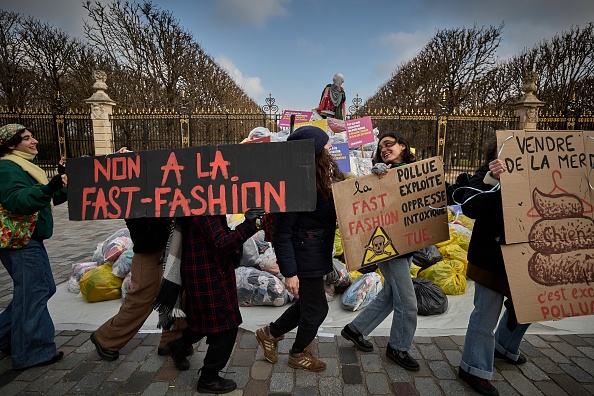 Des activistes tiennent des banderoles alors qu'ils se rassemblent devant des sacs de déchets textiles livrés devant une porte menant au Sénat. (KIRAN RIDLEYKIRAN RIDLEY/AFP via Getty Images)